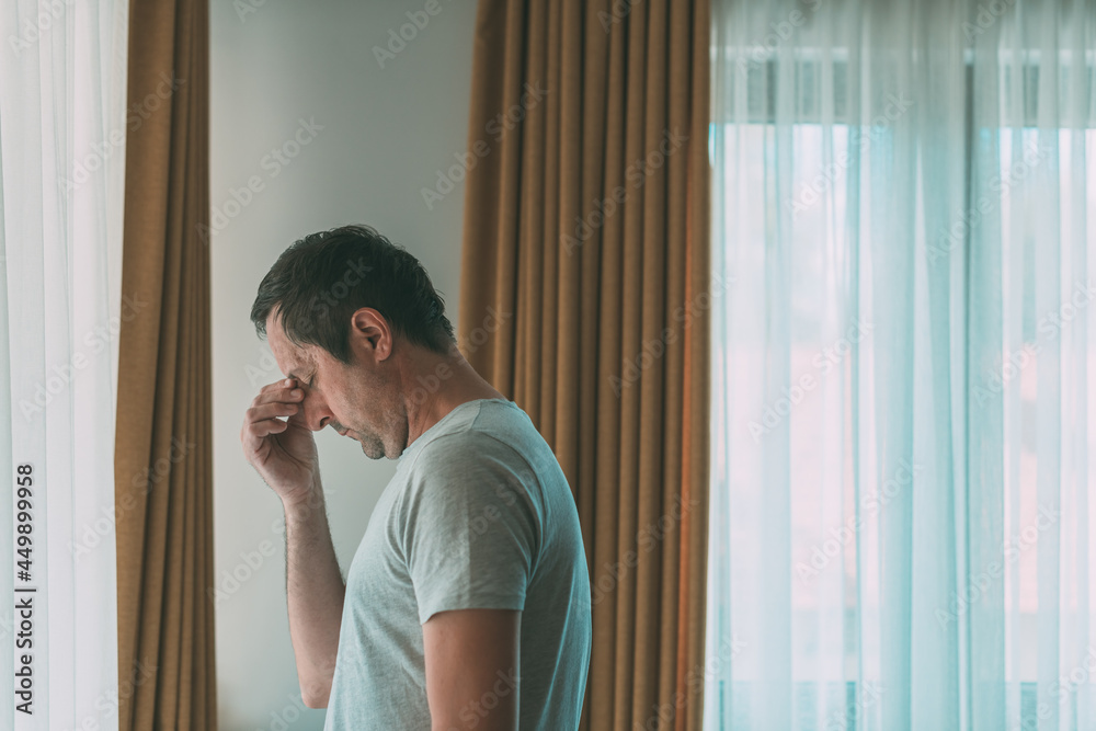 Depressed man is standing by the window. Sad disappointed male person with mental health problems.