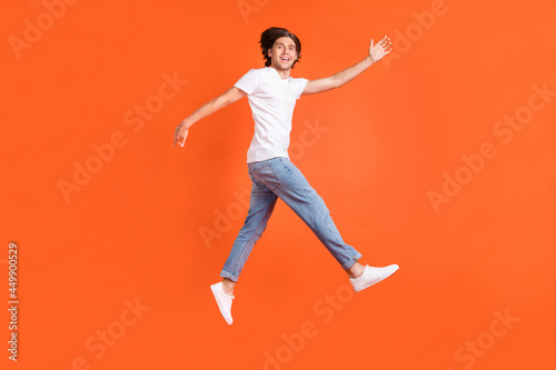 Full size photo of happy cheerful positive man jump up go empty space sale isolated on orange color background