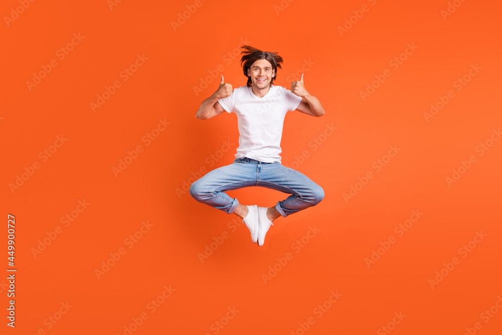 Full length photo of young funky happy man jump up good mood thumbs up isolated on orange color background