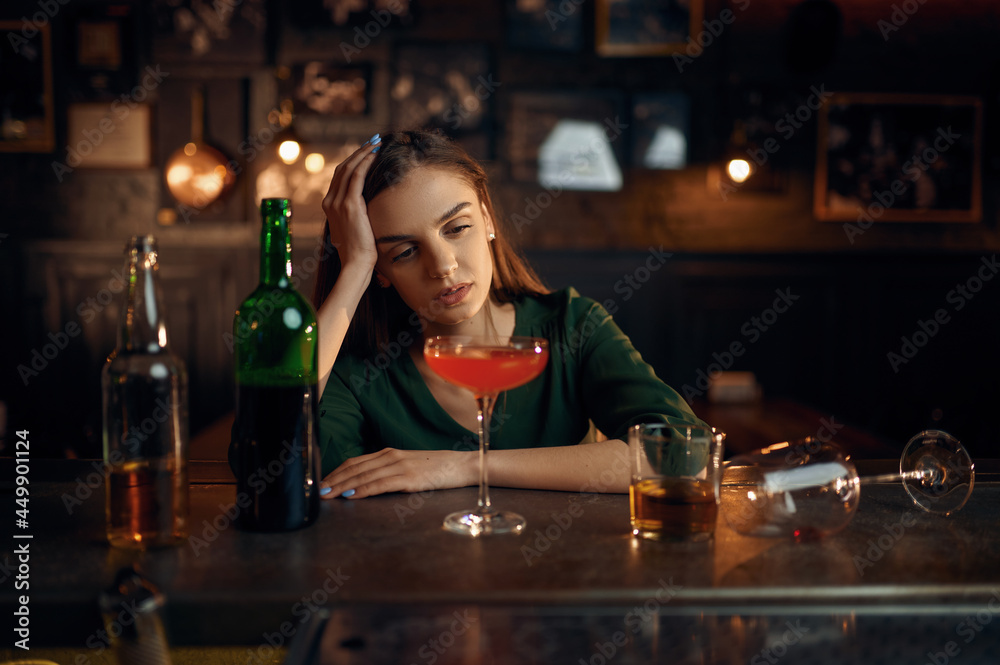 Depressed woman drinks alcohol at counter in bar