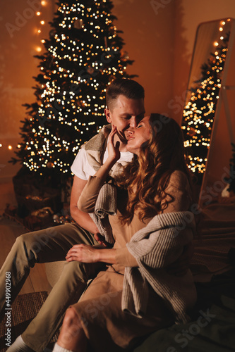 A happy couple in love in elegant outfits hug, kiss, celebrate the Christmas holiday New Year, give each other a gift box in a cozy decorated room at home at night © Елизавета Старкова