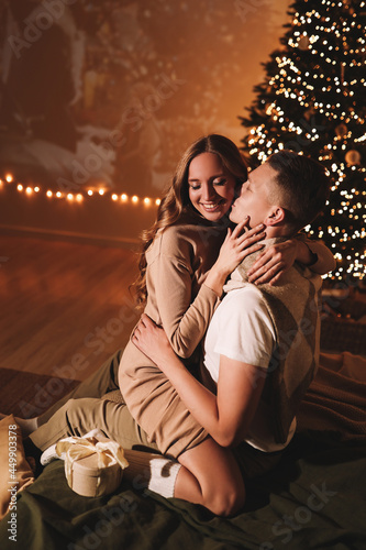 The concept of Christmas. A happy man and a woman in love celebrate the winter New Year holidays at night in a cozy house. A couple in love are kissing hugging together watching a movie eating popcorn