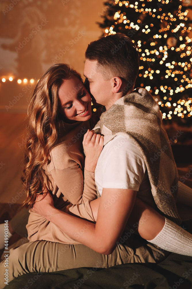 The concept of Christmas. A happy man and a woman in love celebrate the winter New Year holidays at night in a cozy house. A couple in love are kissing hugging together watching a movie eating popcorn The concept of Christmas. A happy man and a woman in love celebrate the winter New Year holidays at night in a cozy house. A couple in love are kissing hugging together watching a movie eating popcorn