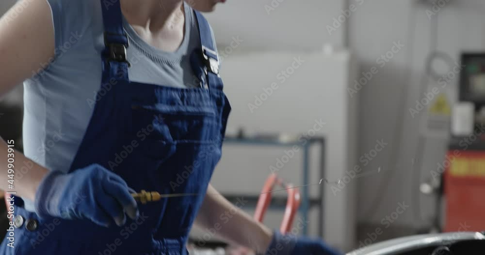 Female mechanic checking a car's engine oil Female mechanic checking a car's engine oil