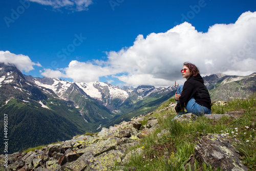 A girl in sunglasses against the background of mountains looks into the distance. Active recreation. A sunny summer day.