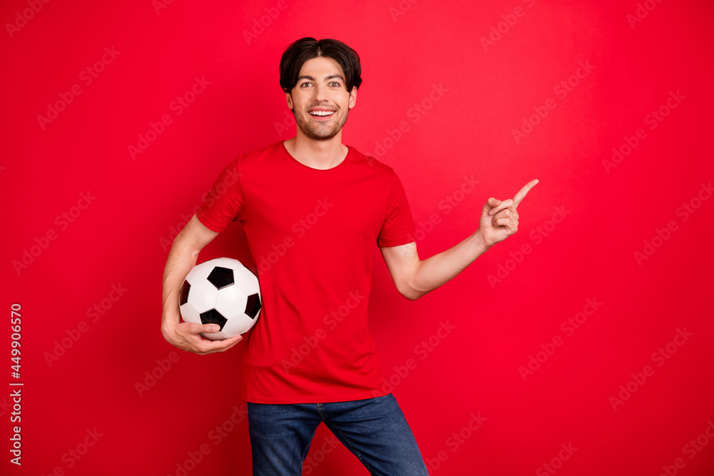 Photo of young man happy positive smile hold soccer ball point finger empty space ad choice decision isolated over red color background Photo of young man happy positive smile hold soccer ball point finger empty space ad choice decision isolated over red color background