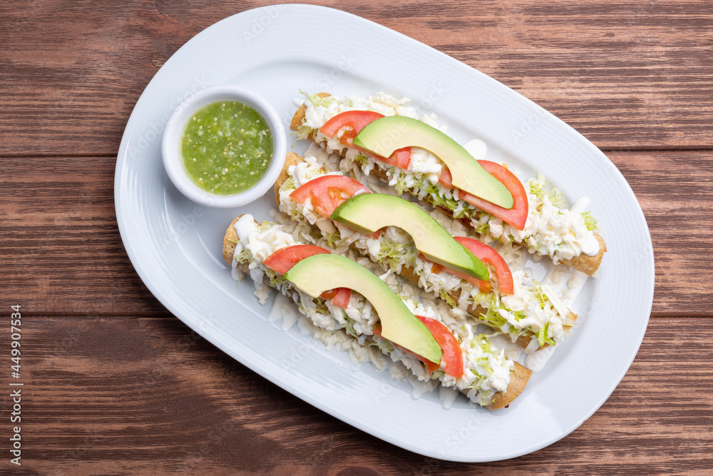 Mexican flutes, golden tacos. Traditional Mexican food. Traditional Mexican tacos with tomato, avocado and green hot sauce. Gourmet mexican food Mexican flutes, golden tacos. Traditional Mexican food. Traditional Mexican tacos with tomato, avocado and green hot sauce. Gourmet mexican food