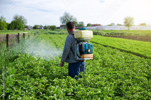 A farmer sprays pesticides on plantation. Use of chemicals for protection of cultivated plants from insects and fungal infections. Agriculture and agro industry. Farm work. Pesticides and fungicides photo