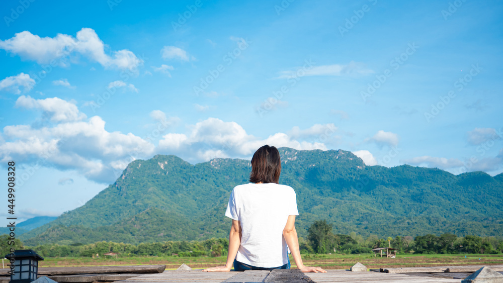 girl wearing a casual t-shirt Sit on a wooden walkway, see nature, mountains, rice fields, fresh air. and the morning sun bright blue sky white clouds