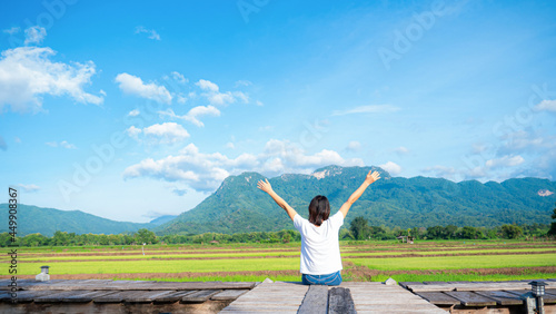 The girl held up two hands and breathed fresh. show independent symptoms Sit by a wooden bridge on a rice field, nature, clear air. Grasslands, mountains, and clear skies.