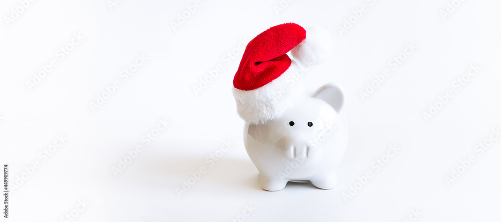 Creative composition with piggy bank in Santa’s hat on white background long banner format. Christmas bank promotions and deposits concept. Festive New Year and Christmas shopping. Creative composition with piggy bank in Santa’s hat on white background long banner format. Christmas bank promotions and deposits concept. Festive New Year and Christmas shopping.