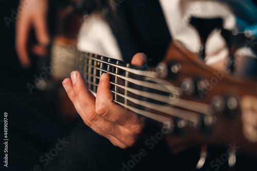 Closeup of male fingers playing the fretboard of a 5 stringed bass guitar