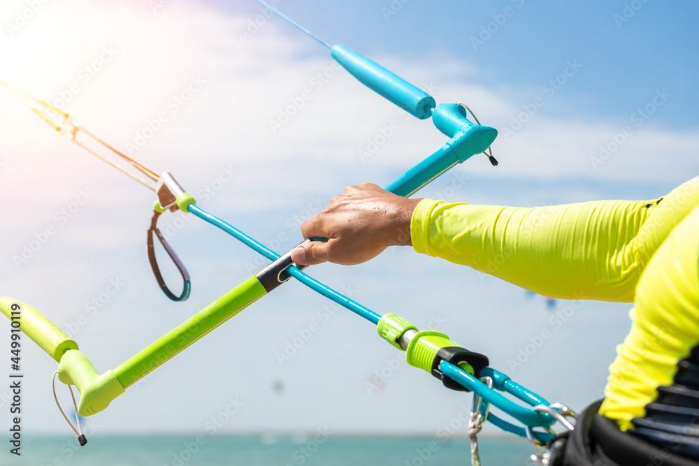 Young adult caucasian fit male person adjust kite surf board bar in sun uv protection suit on bright sunny day against blue sky at sea or ocean shore. Watersport adrenaline fun adventure acitivity Young adult caucasian fit male person adjust kite surf board bar in sun uv protection suit on bright sunny day against blue sky at sea or ocean shore. Watersport adrenaline fun adventure acitivity