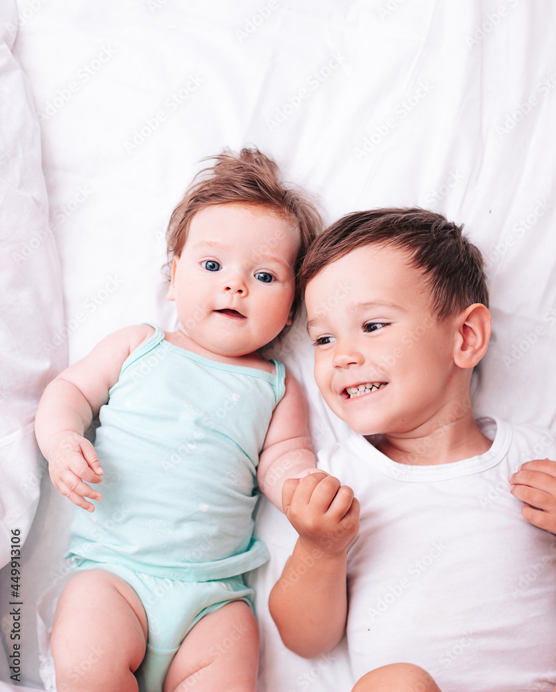 happy little brother hugs his little sister lying on a white blanket happy little brother hugs his little sister lying on a white blanket