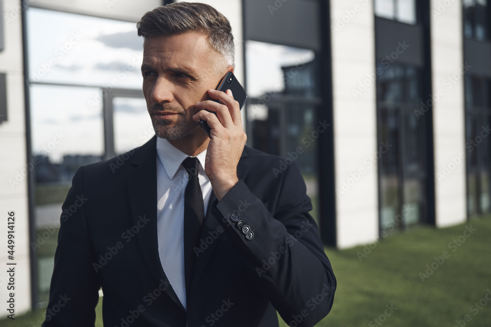 Confident mature businessman talking on mobile phone while standing near office building Confident mature businessman talking on mobile phone while standing near office building