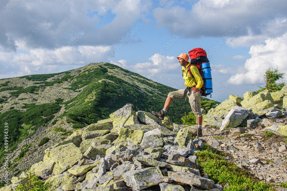 A male tourist with a large backpack climbs a mountain stone path high in the Carpathian Gorgan. Ukraine