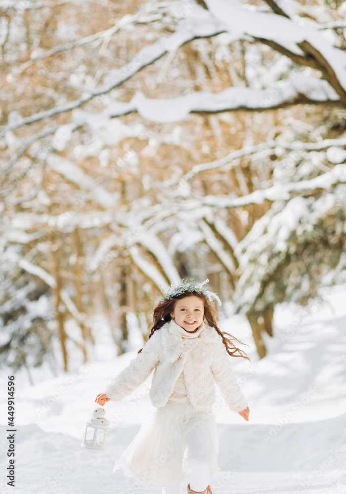 Happy little girl runs on a forest path with a lantern in her hand. Christmas time. Sunny winter day. Happy little girl runs on a forest path with a lantern in her hand. Christmas time. Sunny winter day.