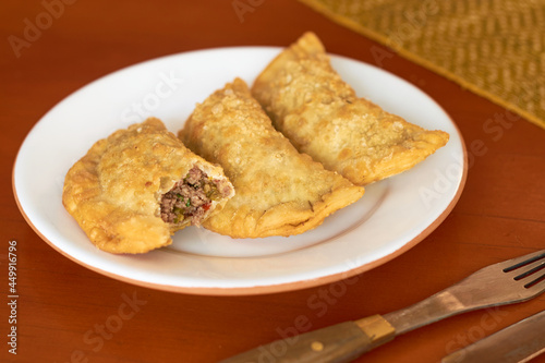 Half-eaten empanadas on a porcelain plate, on a wooden table. Argentine gastronomy concept.