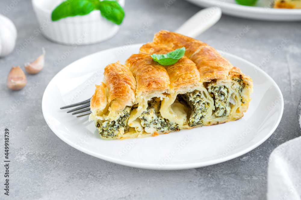Greek pie spanakopita with feta cheese and spinach on a white plate on a gray concrete background. Copy space. Greek pie spanakopita with feta cheese and spinach on a white plate on a gray concrete background. Copy space.