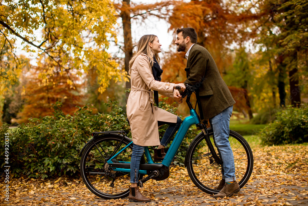 Fototapeta premium Young couple in the autumn park with electrical bicycle