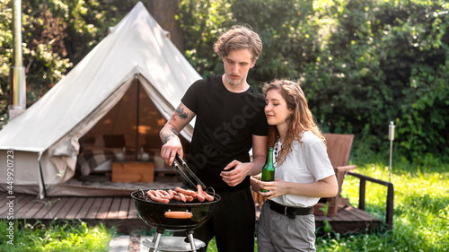 Young couple frying meat on the grill and drinking beer