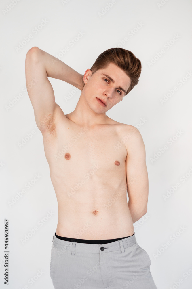 Fashion model young attractive man with naked torso with thin body with trendy hairstyle with beautiful sexy cheekbones in pants posing near white wall in studio.Handsome half-naked guy stands in room Fashion model young attractive man with naked torso with thin body with trendy hairstyle with beautiful sexy cheekbones in pants posing near white wall in studio.Handsome half-naked guy stands in room