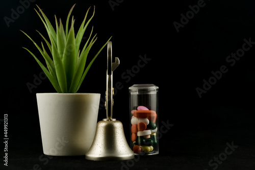Medicine tablets and capsules in glass tube container with green plant and hand bell decoration