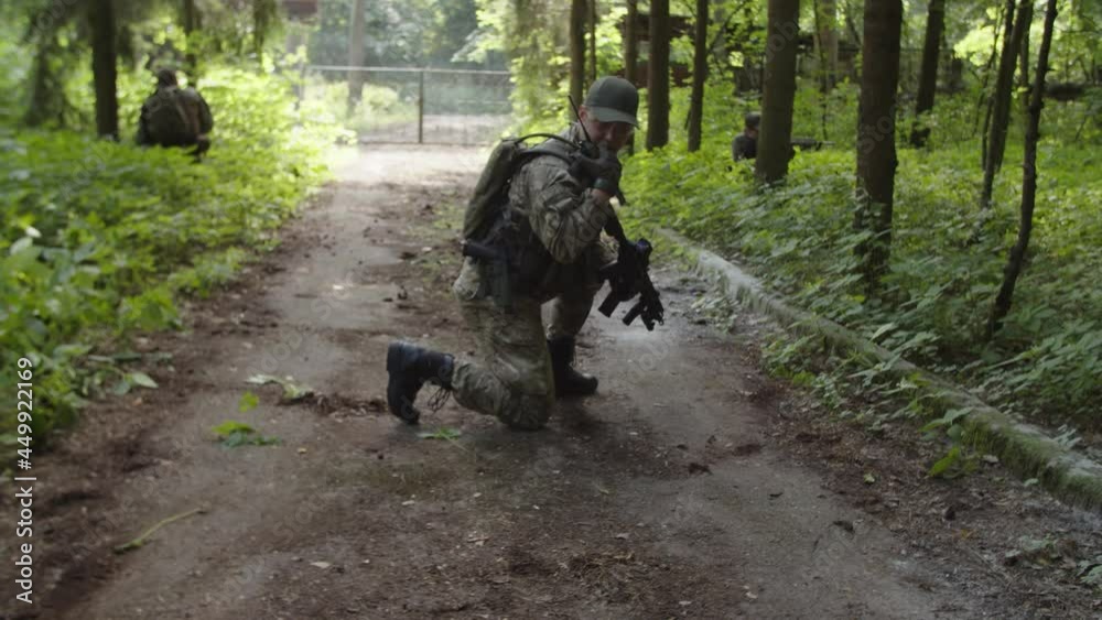 Armed soldier in camouflage using radio communication, calling evacuation transport while combat medic providing emergency medical treatment to injured soldier during danger military mission in forest