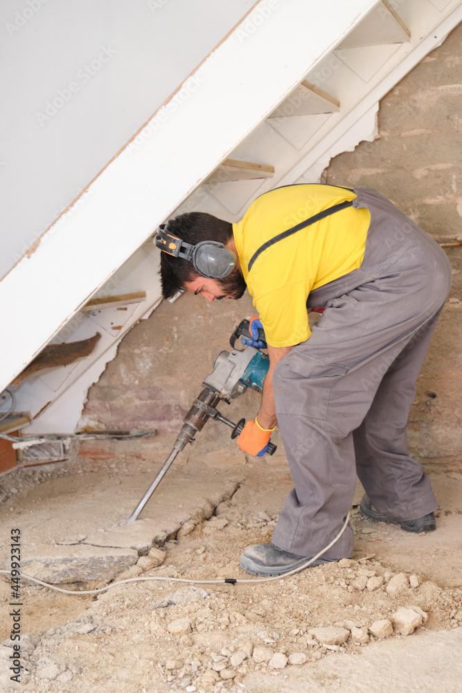 Young builder breaking up a house floor with a jackhammer. Young builder breaking up a house floor with a jackhammer.