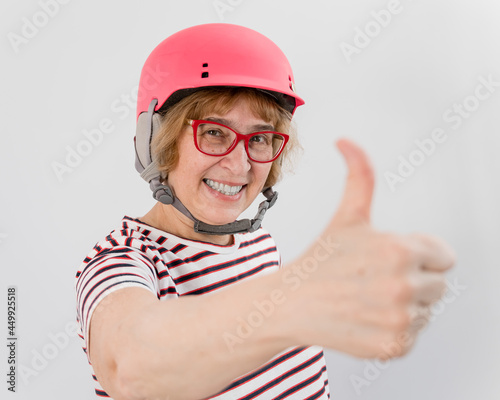 Elderly woman in ski helmet showing thumb up on white background.