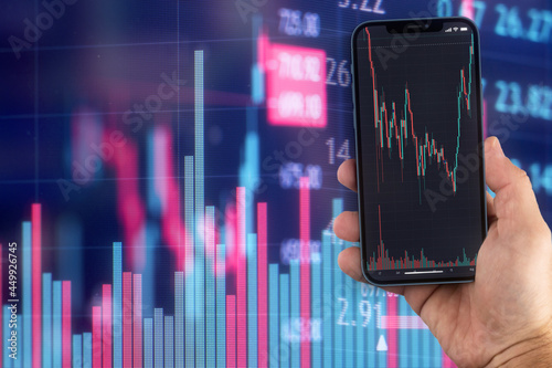 Male hand holding a smartphone with financial stock market graph. Stock Exchange. Graphics in the background.