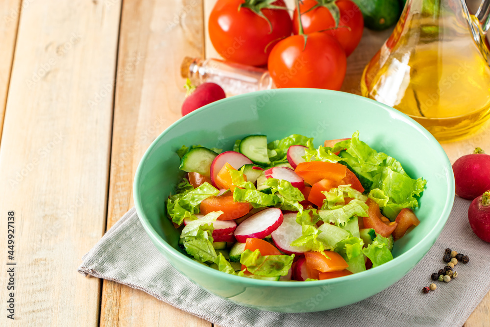Fresh vegetable salad with olive oil in ceramic bowl on wooden background. Seasonal summer dish of tomatoes, cucumbers and radishes.