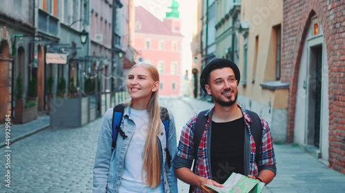 Happy couple of tourists with map walking on central street of old European city. They looking around and smiling.