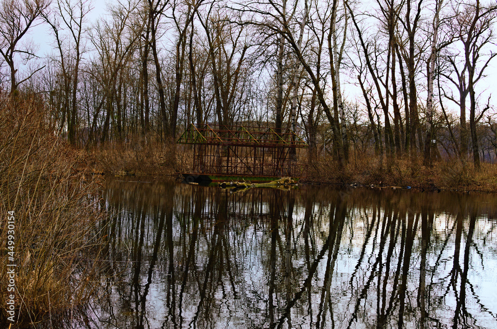 Abandoned ruins skeleton of barge near the shore of lake. Bare trees in the background. Trees reflected in tranquil water. Concept of landscape and nature Abandoned ruins skeleton of barge near the shore of lake. Bare trees in the background. Trees reflected in tranquil water. Concept of landscape and nature