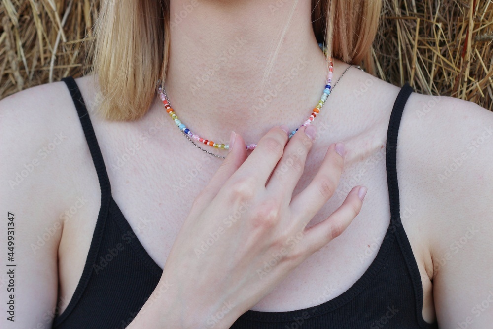 Body details of a beautiful young woman. Shoulder, collarbone and neck. A hand touches the skin and chain of multi-colored beads.