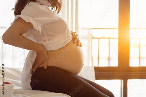 pregnant woman is enjoying herself waiting for her delivery and is relaxing on the white sofa by the window. Happy concept of pregnant women and looking forward to the day seeing the baby face.