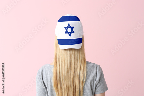 Young woman in stylish cap with Israeli flag on color background