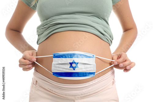 Pregnant woman holding medical mask with painted Israeli flag on white background photo