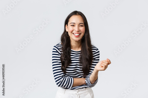 Lifestyle, people emotions and casual concept. Carefree happy outgoing asian woman having fun talking to people, laughing and smiling upbeat, standing white background cheerful
