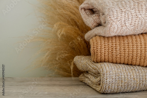 Bunch of knitted warm pastel color sweaters with different knitting patterns folded in stack, clearly visible texture. Stylish fall-winter season knitwear clothing. Close up, copy space for text.