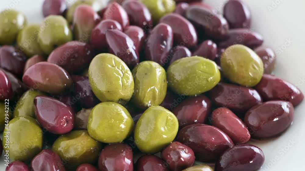 Olives in olive oil spin around themselves on white background. Rotating shot. Mediterranean organic fresh healthy food ingredient, slow motion, close up, macro Olives in olive oil spin around themselves on white background. Rotating shot. Mediterranean organic fresh healthy food ingredient, slow motion, close up, macro