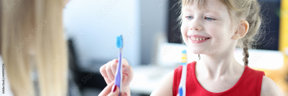 Dentist shows little girl two toothbrushes closeup Dentist shows little girl two toothbrushes closeup