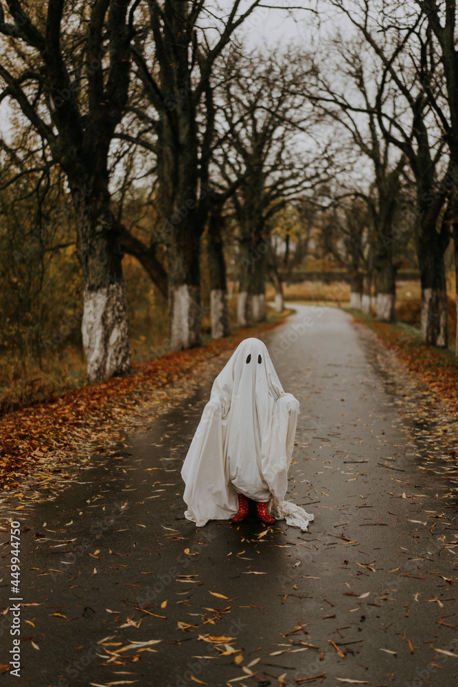 little ghost standing on the road in red boots. Autumn halloween