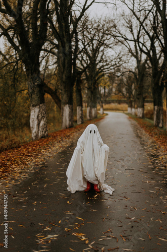 little ghost standing on the road in red boots. Autumn halloween