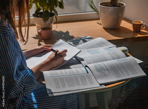 Canvas Print Female hands writing with pen in notebook, taking notes, studying with academic textbook, close up