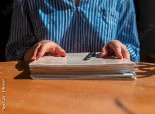 Closeup of female hands with stack of documents on wooden table.