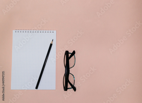 white open notebook in a cage with a black pencil for notes and reading glasses on a pink background with place for text