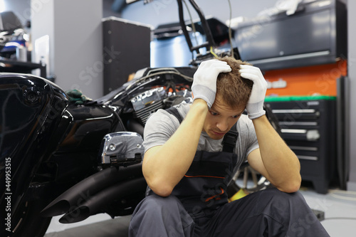 Master locksmith with headache sits near motorcycle at service station