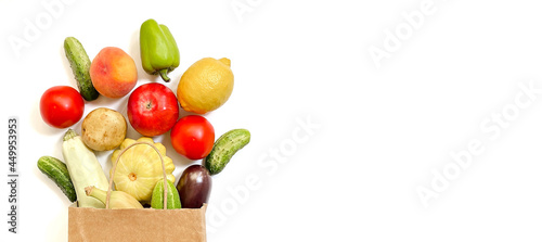 Fototapeta Naklejka Na Ścianę i Meble -  A paper shopping bag from which vegetables and fruits fall out, namely tomato, cucumber, squash, pepper, lemon, eggplant, zucchini, banana, apple, peach on white background.