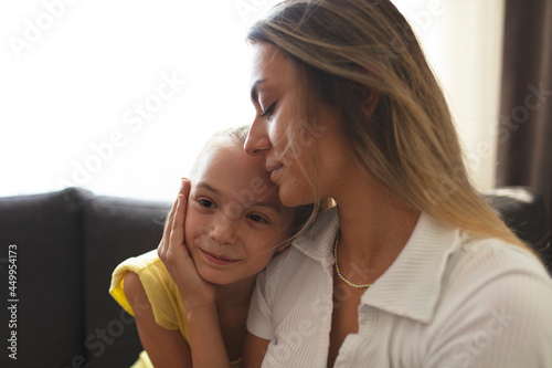 Close up loving young mother with closed eyes hugging adorable little daughter, sitting on cozy couch, caring mum and cute girl enjoying tender moment together, good family relationship concept